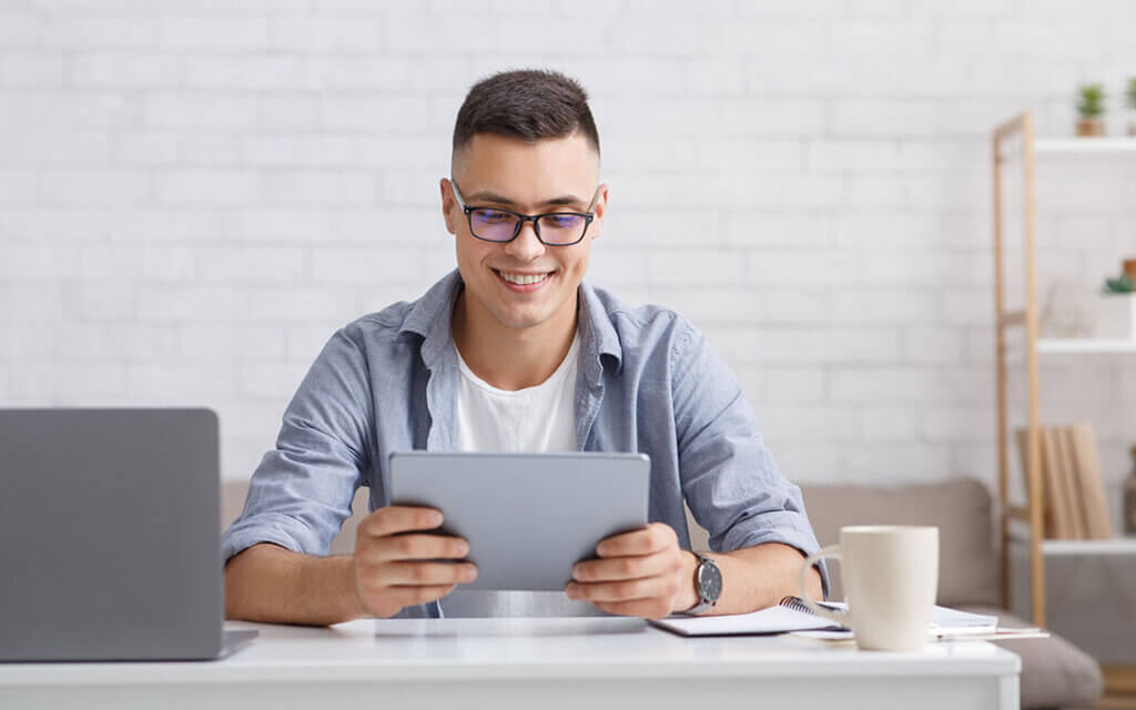 Bewerbung mit ChatGPT: Tipps für Schüler*innen 1 Bewerbung mit ChatGPT: ein junger Mann sitzt mit Tablet und Laptop am Schreibtisch