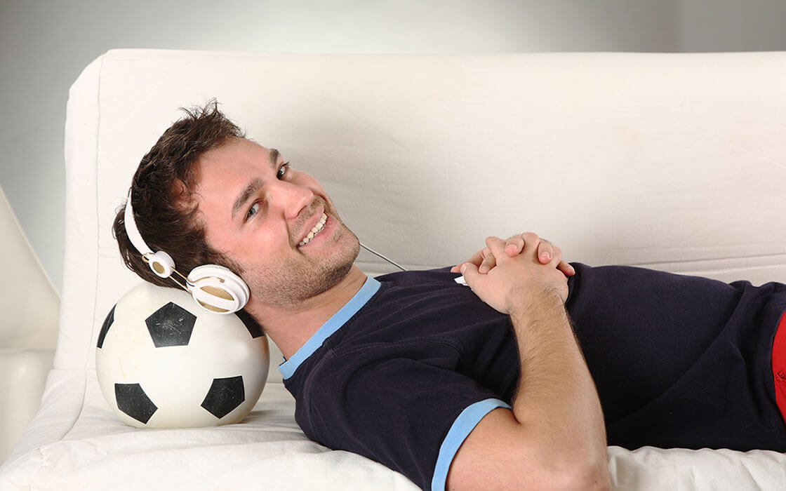 Was ist ein Traumberuf? Ein junger Mann liegt mit Kopfhörern auf den Sofa, den Kopf auf einen Fußball gestützt, und lächelt