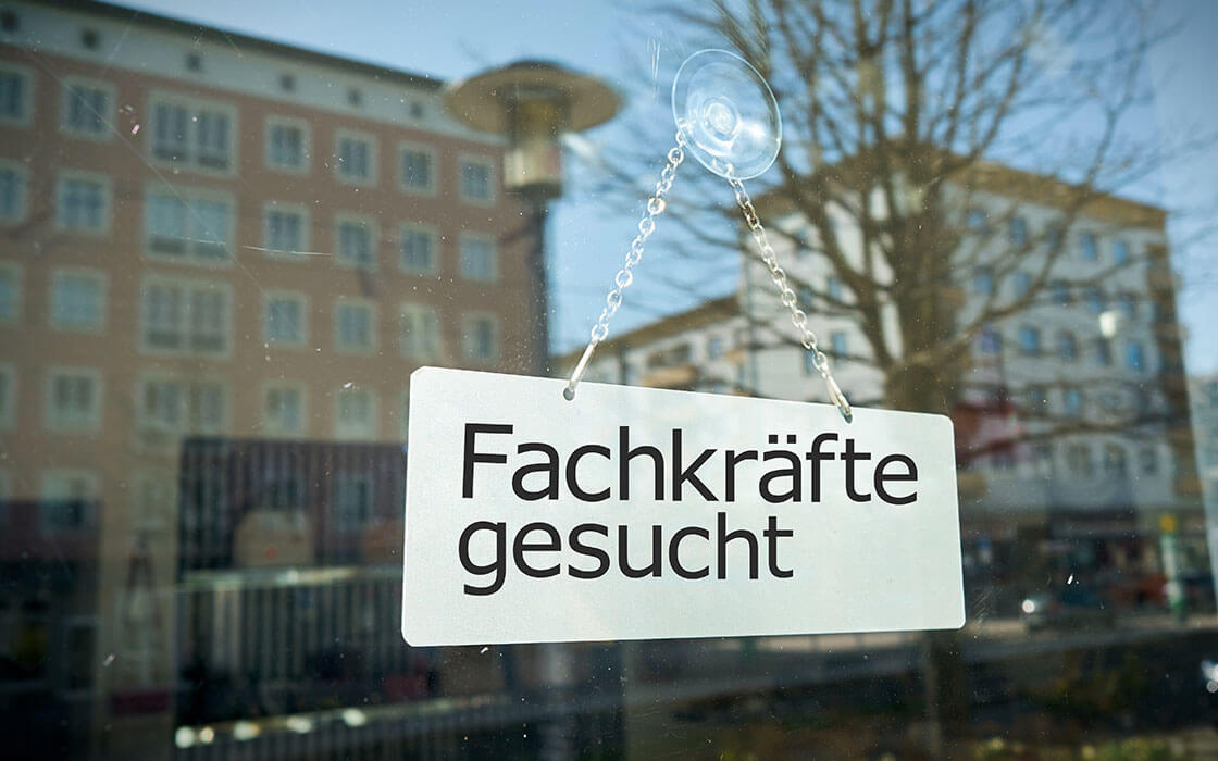 Fachkräftemangel: Aushang eines Schilds mit der Aufschrift Fachkräfte gesucht am Fenster eines Betriebs in einer Stadt